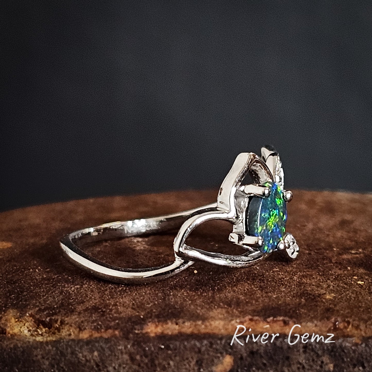 Silver ring with a colorful gemstone on a iron shoe anvil, branded 'River Gemz'.