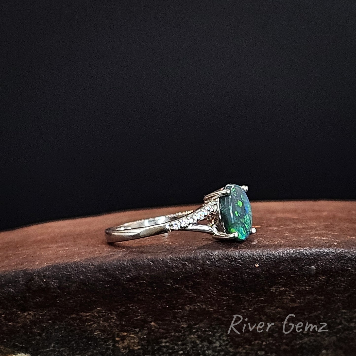 Green and blue genuine black opal claw set in silver ring with split shoulders accented with topaz stones.