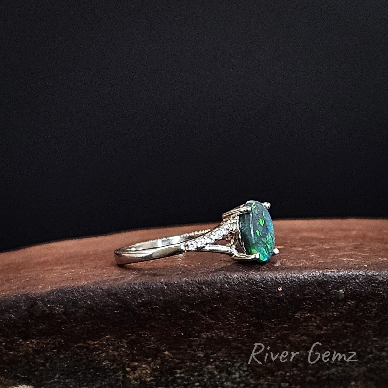 Green and blue genuine black opal claw set in silver ring with split shoulders accented with topaz stones.