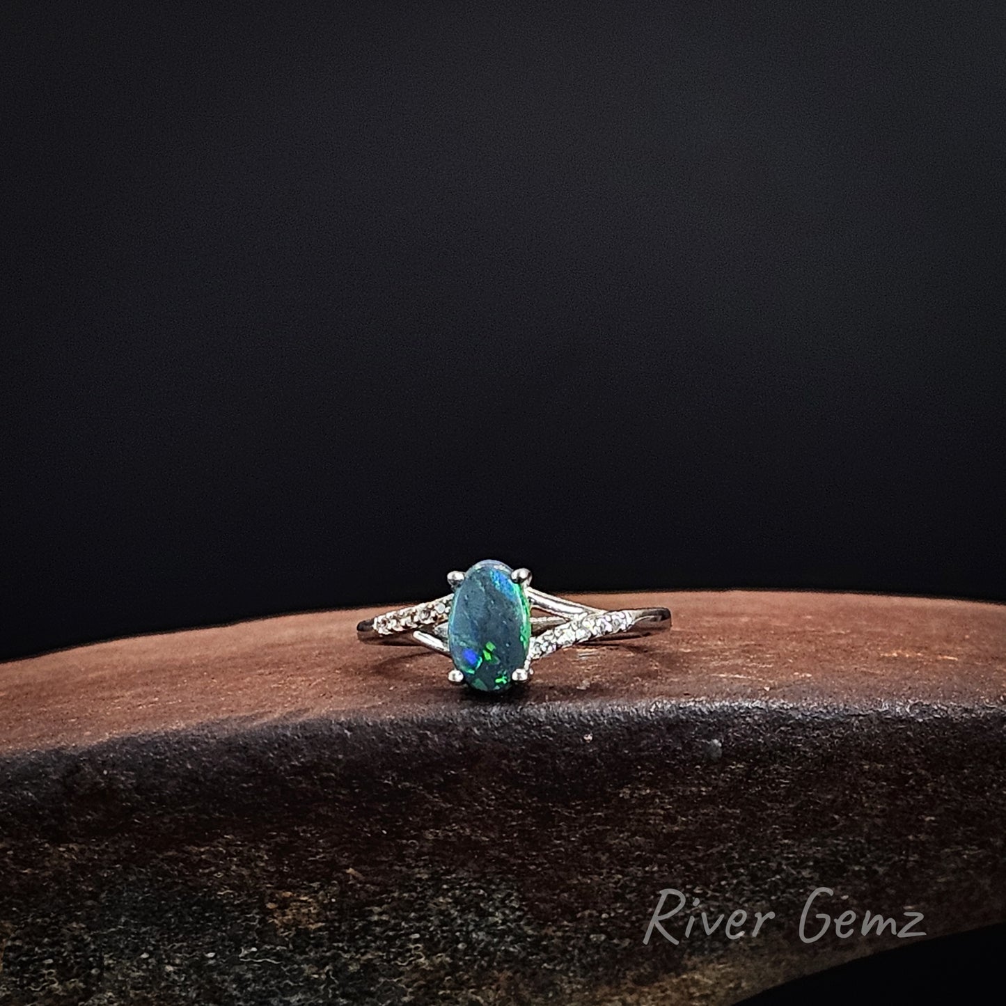 Oval shaped black opal with 6 white topaz stones on each shoulder of the sterling silver ring.