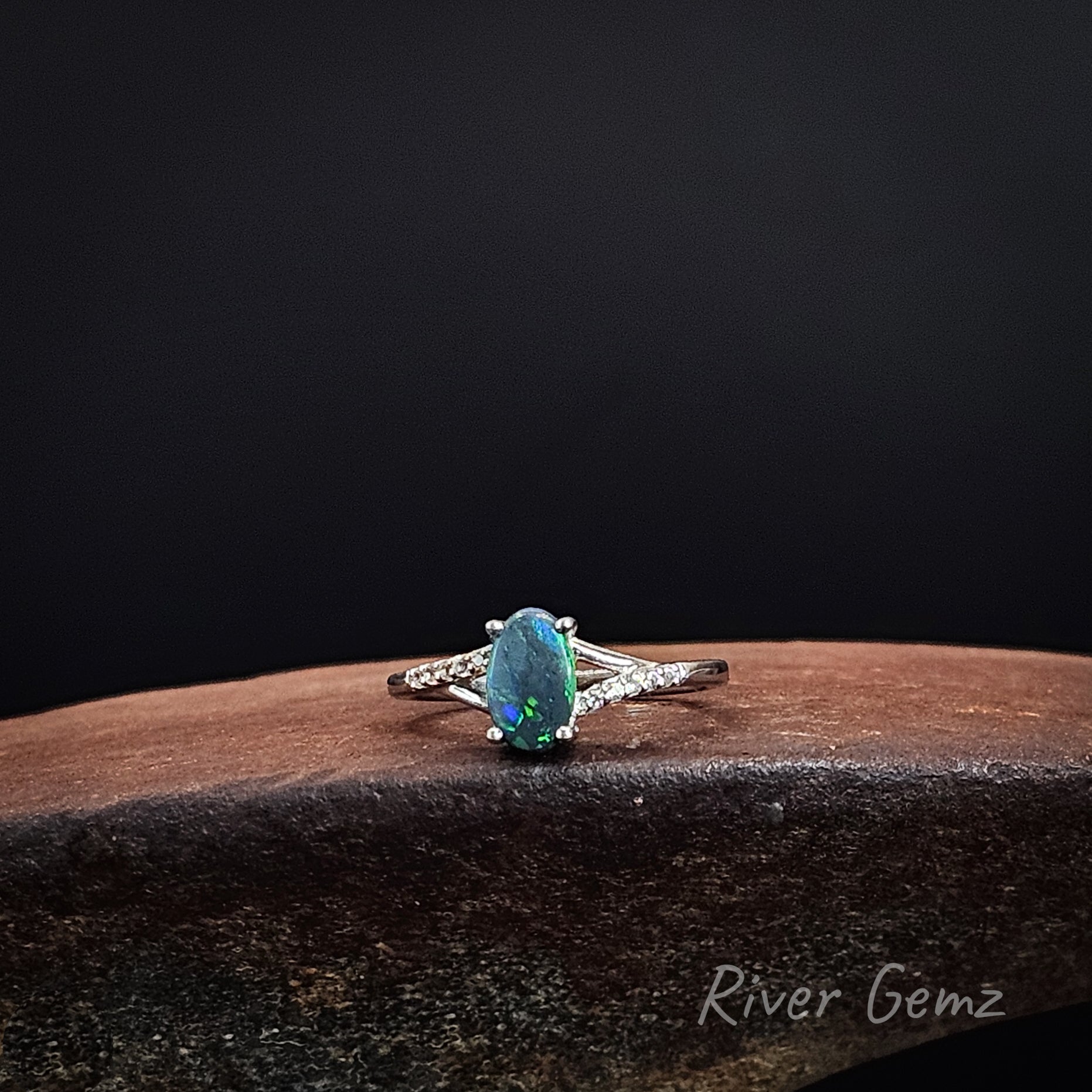 Oval shaped black opal with 6 white topaz stones on each shoulder of the sterling silver ring.