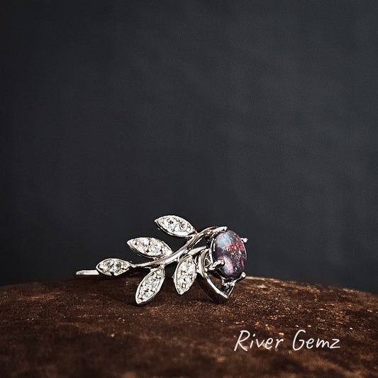 Silver leaf-shaped ring with a central black opal on a dark background, branded 'River Gemz'.