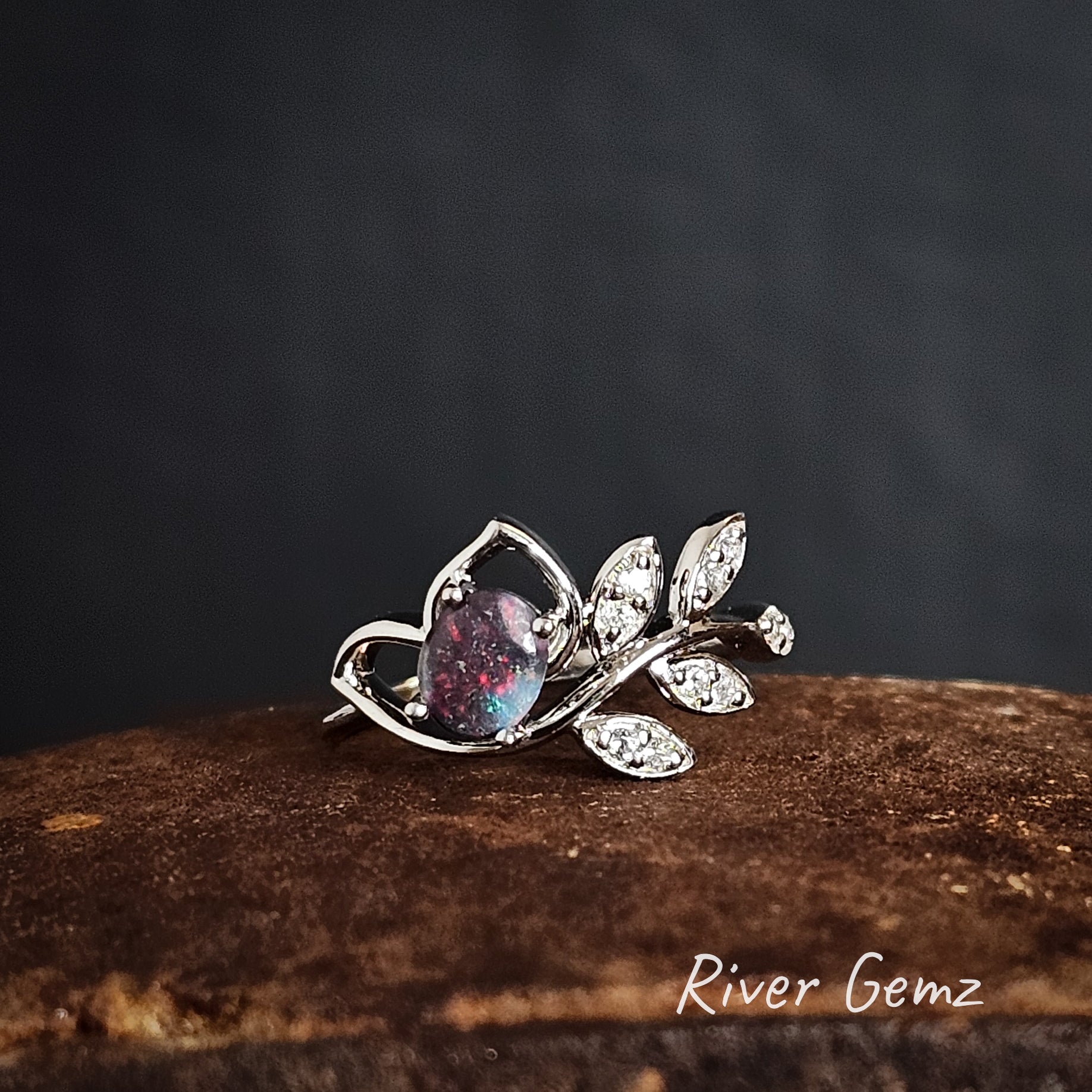 Silver ring with a multi-coloured black opal on a iron shoe anvil, branded 'River Gemz'.