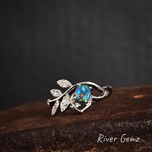 Silver ring with a multi-coloured gemstone and leaf design with white topaz stones in the leaves on a dark surface, branded 'River Gemz'.
