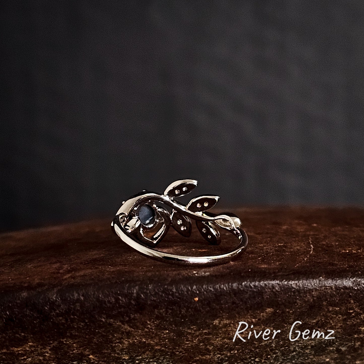 Rear of silver ring shows the dark tone of the included black opal on a cast iron shoe anvil, branded 'River Gemz'.
