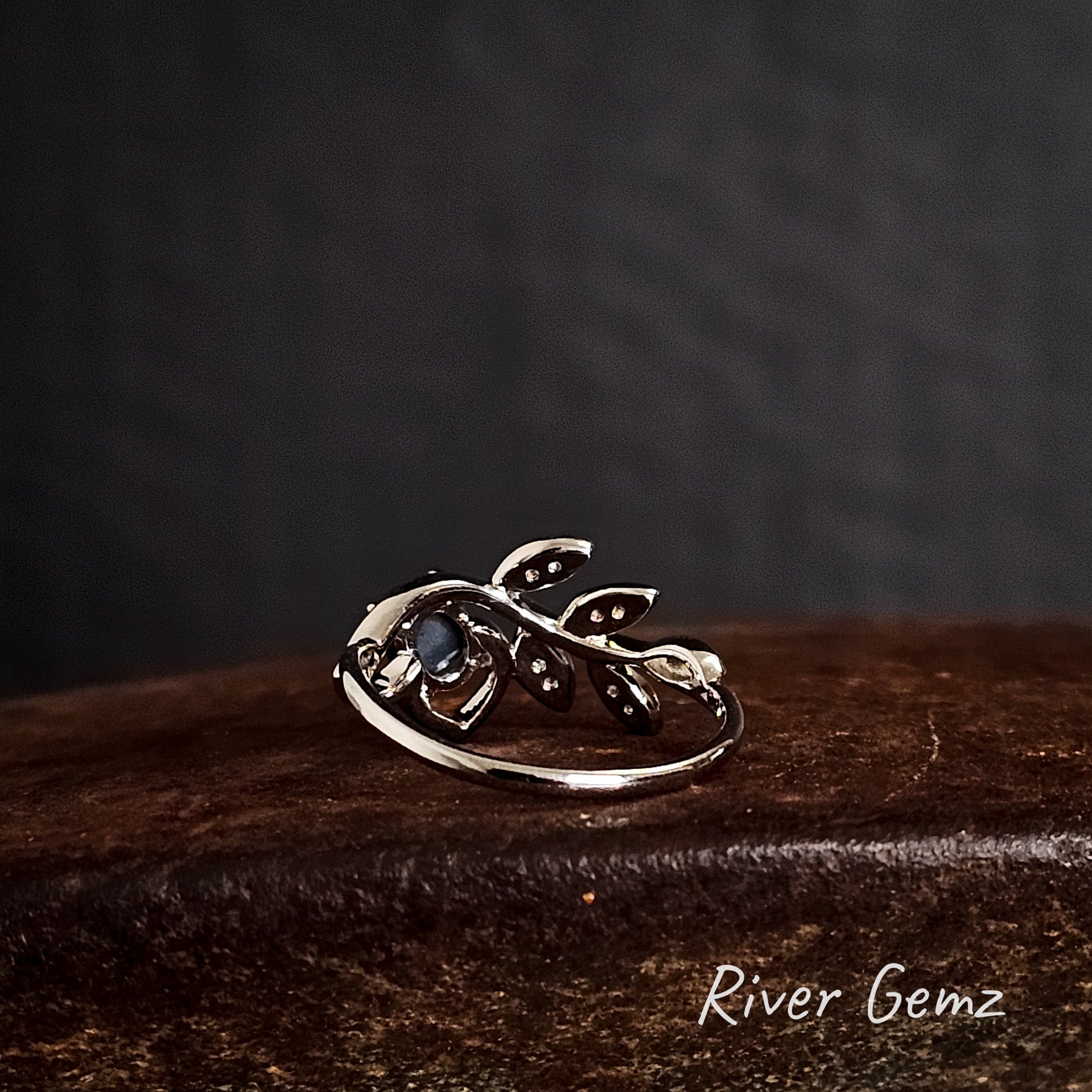 Rear of silver ring shows the dark tone of the included black opal on a cast iron shoe anvil, branded 'River Gemz'.