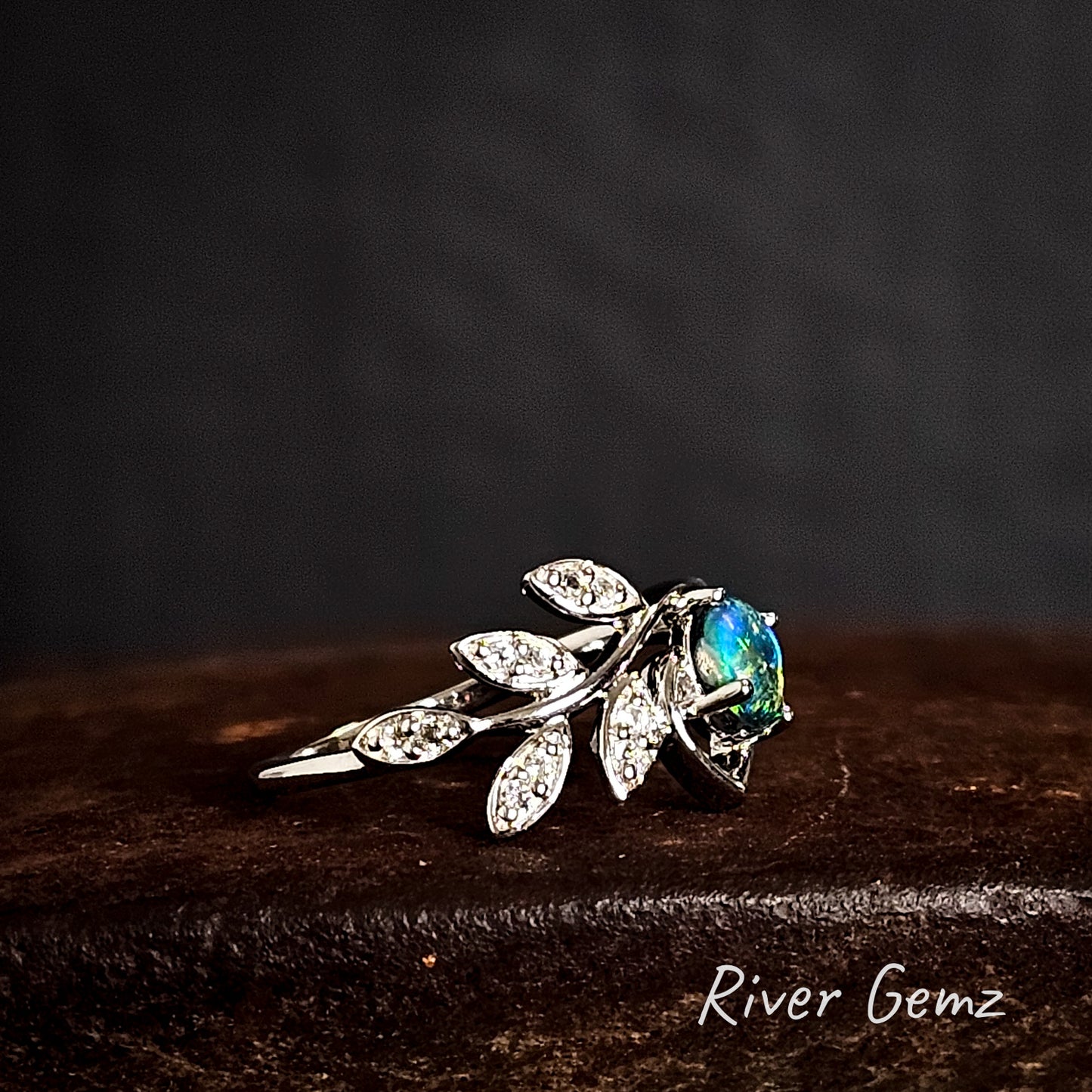 Silver leaf-shaped ring with a claw set dark opal on a dark background, branded 'River Gemz'.