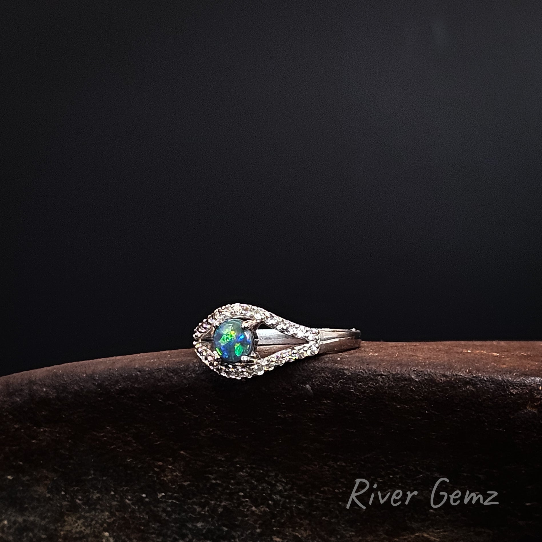 Round dark opal claw set in sterling silver ring with channel set white topaz stones above and below the opal.