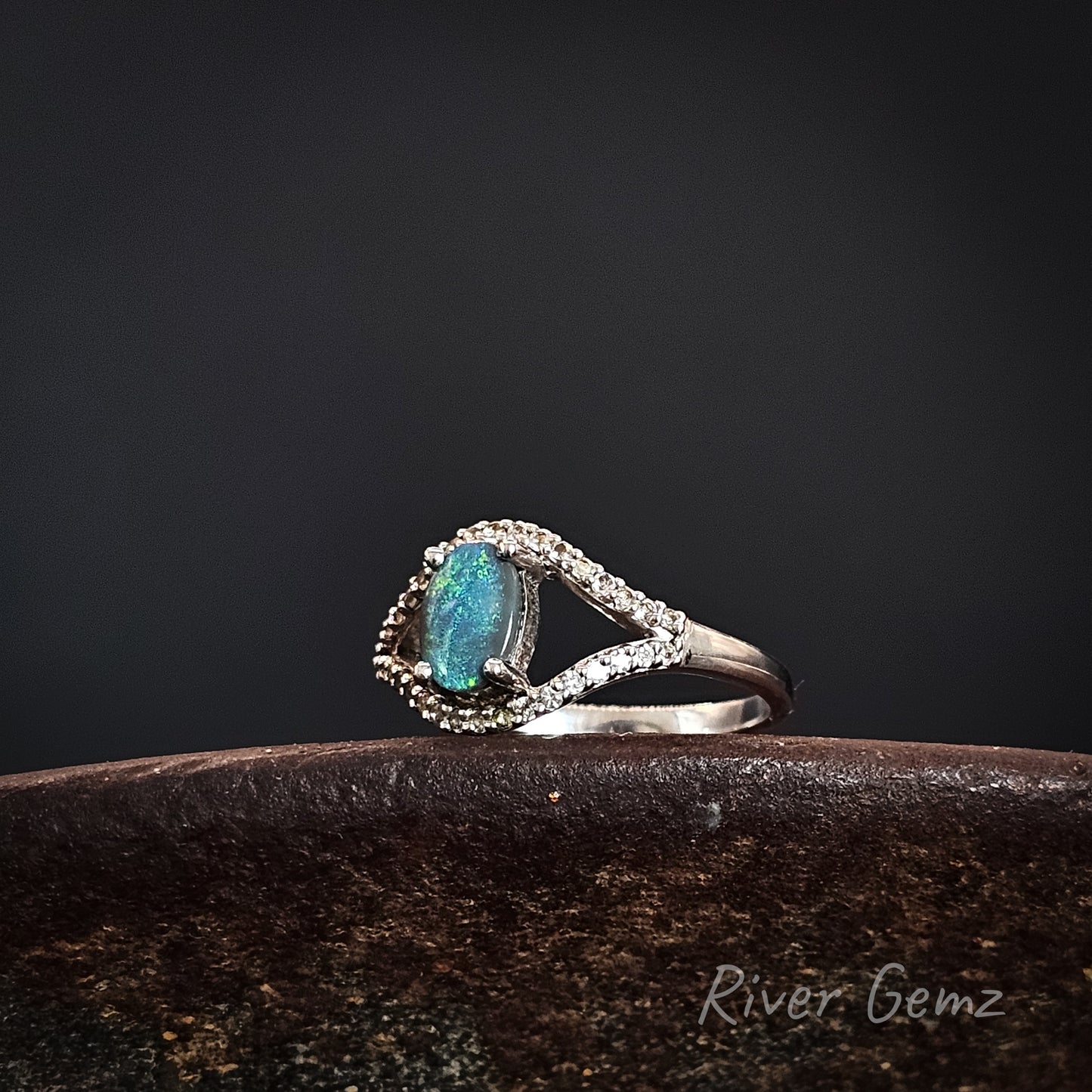 Ring with an oval shaped green gemstone on a dark background.