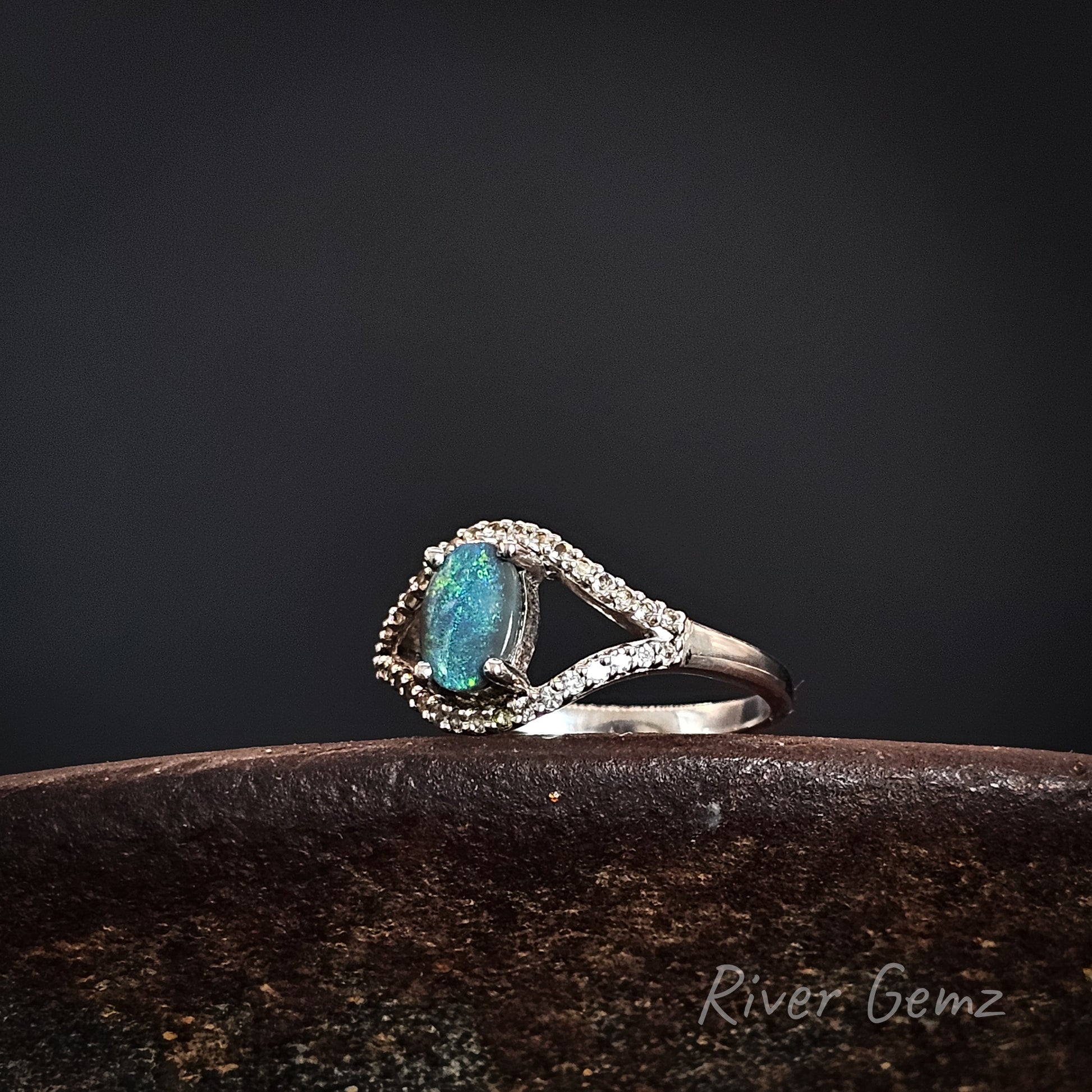 Ring with an oval shaped green gemstone on a dark background.