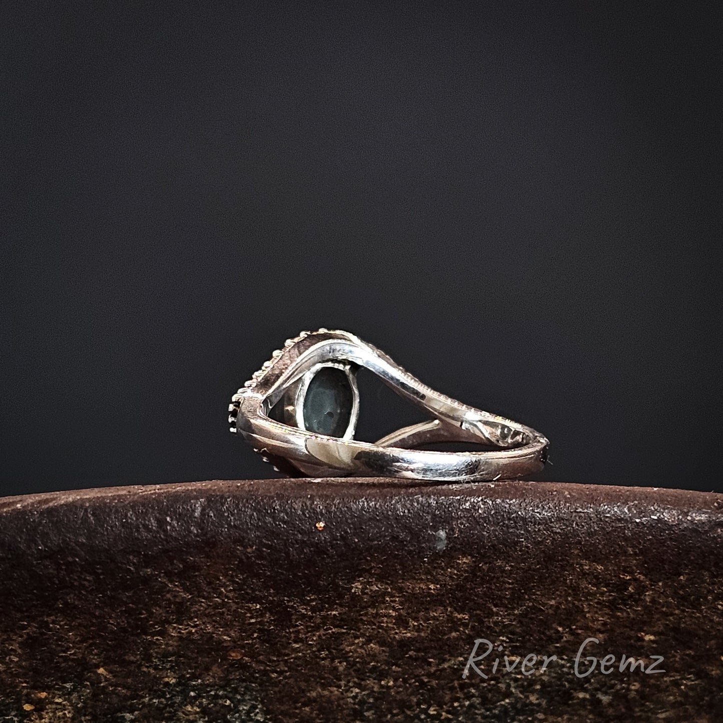 Rear view of the silver ring shows the dark base tone of the black opal on a dark surface, branded 'River Gemz'.