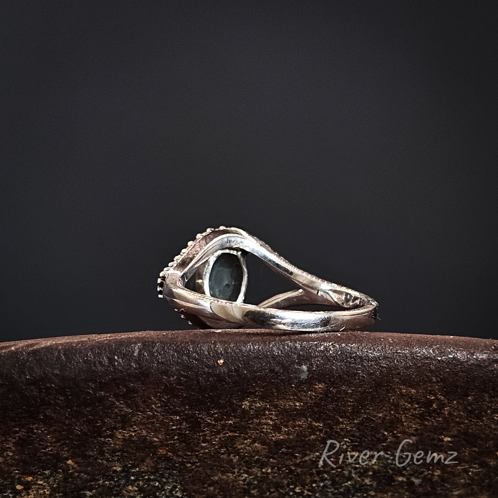 Rear view of the silver ring shows the dark base tone of the black opal on a dark surface, branded 'River Gemz'.