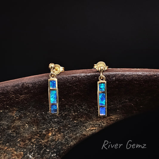Three rectangular shaped blue and green opals channel set in stud earrings that dangle against a black back ground with 'River Gemz' watermark in the bottom right hand corner.
