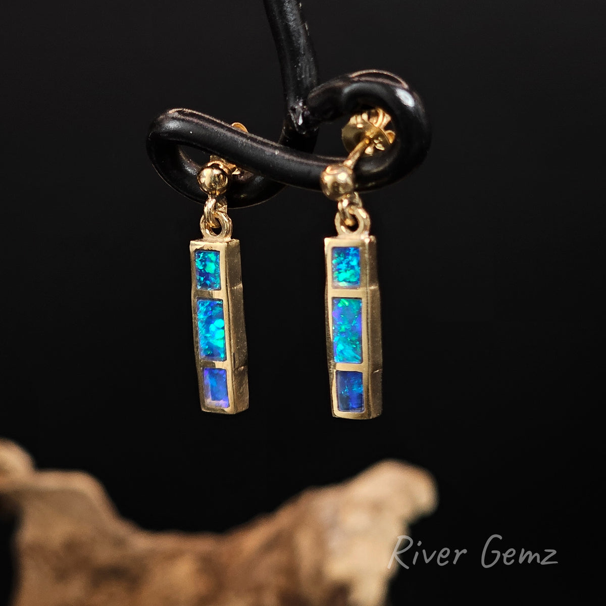 Three rectangular shaped blue and green opals channel set in stud earrings that dangle against a black back ground with 'River Gemz' watermark in the bottom right hand corner.