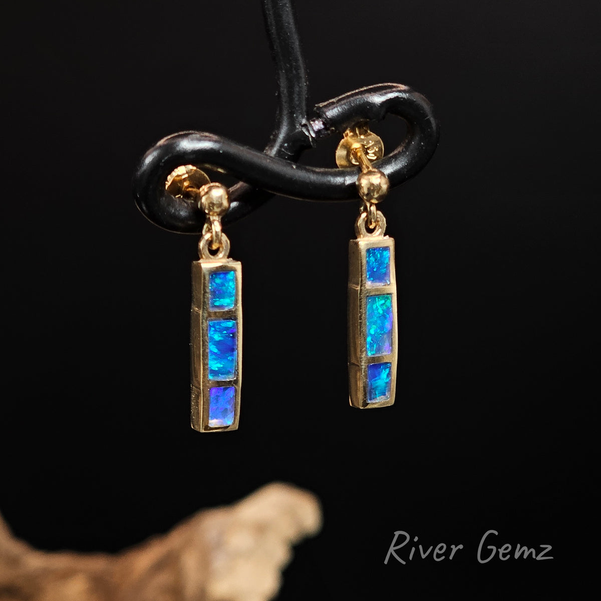Three rectangular shaped blue and green opals channel set in stud earrings that dangle against a black back ground with 'River Gemz' watermark in the bottom right hand corner.