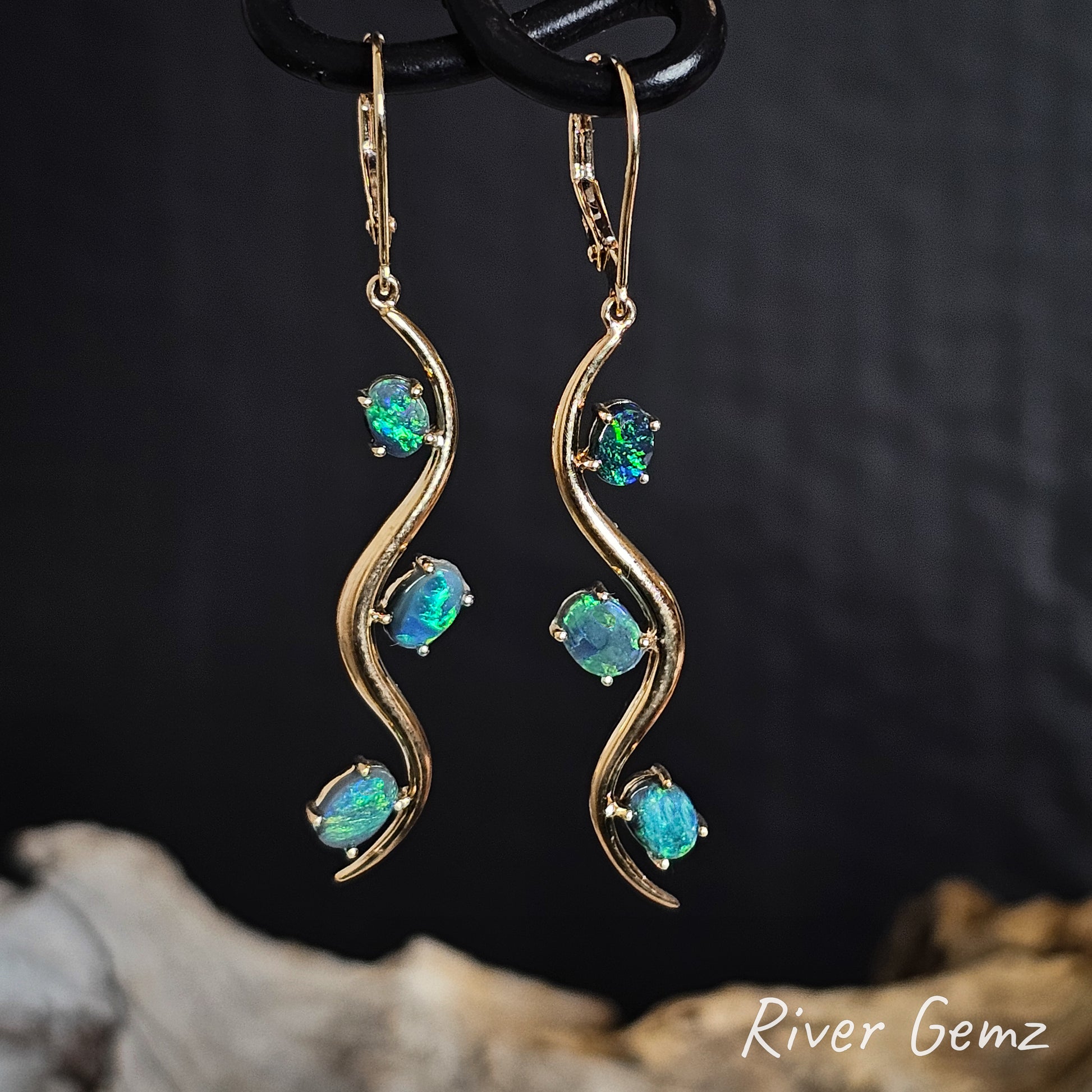Gold earrings with oval shaped green black opals on a dark background.