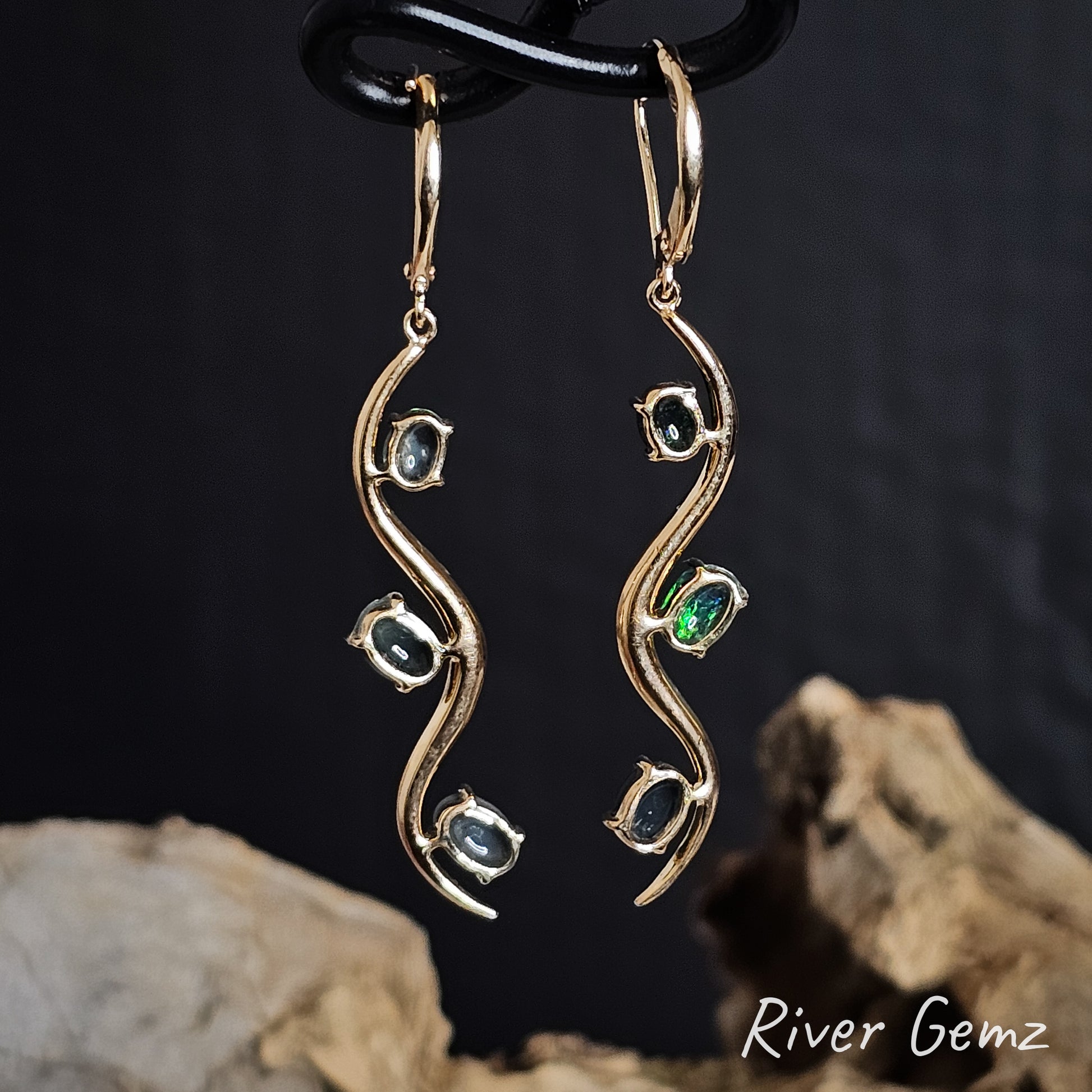 Back of gold earrings showing the dark base tone of the 3 black opals on a dark background