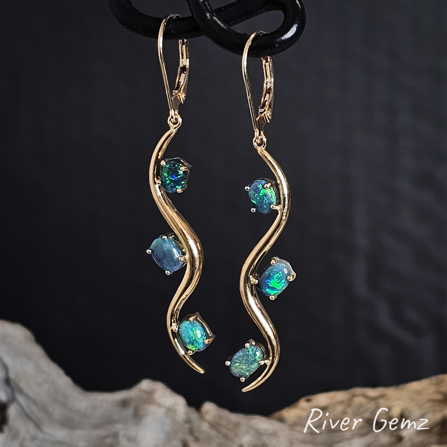 Gold hook earrings with 3 turquoise black opals on a dark background