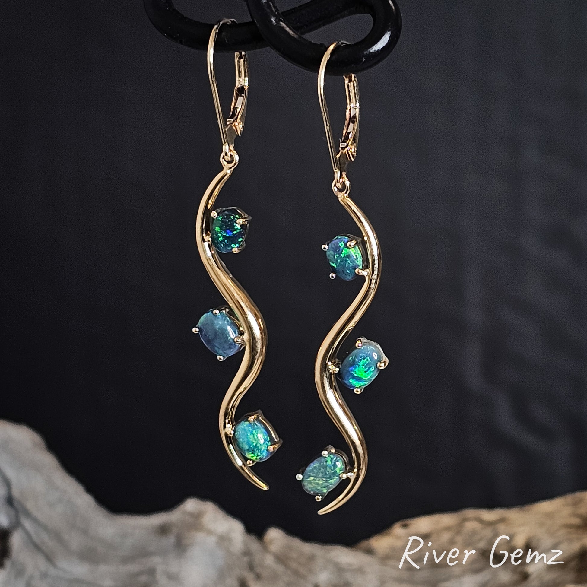 Gold hook earrings with 3 turquoise black opals on a dark background