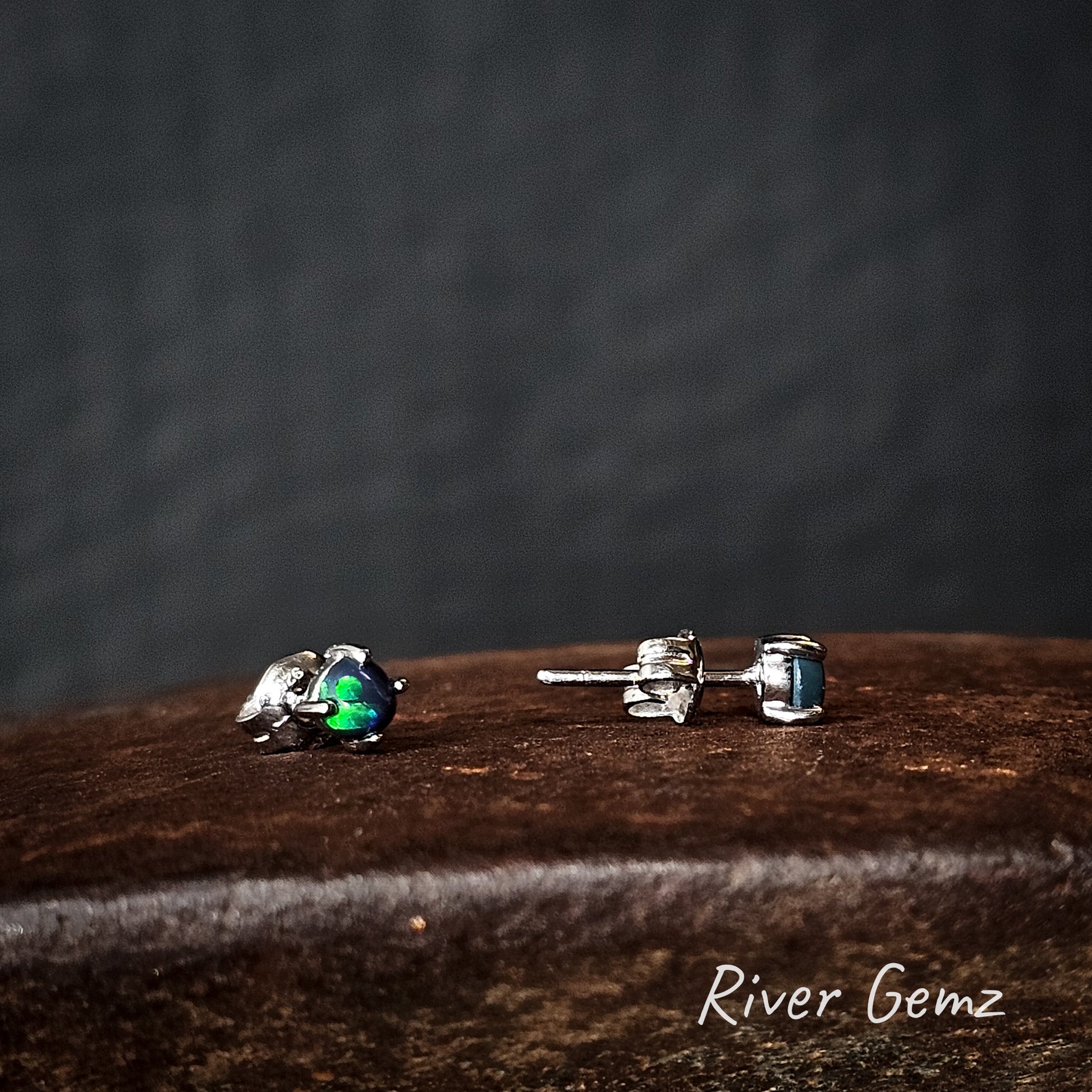 Pair of silver earrings with green gemstones, one stud is shown sideways and the other front on.
