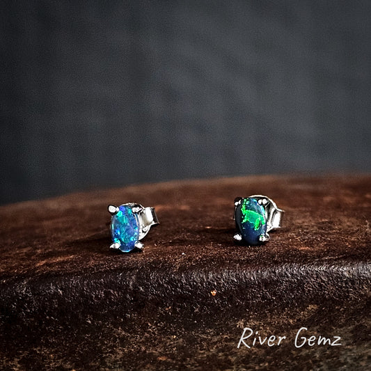 Pair of oval shaped black opal sterling silver stud earrings on a dark brown surface with 'River Gemz' branding.