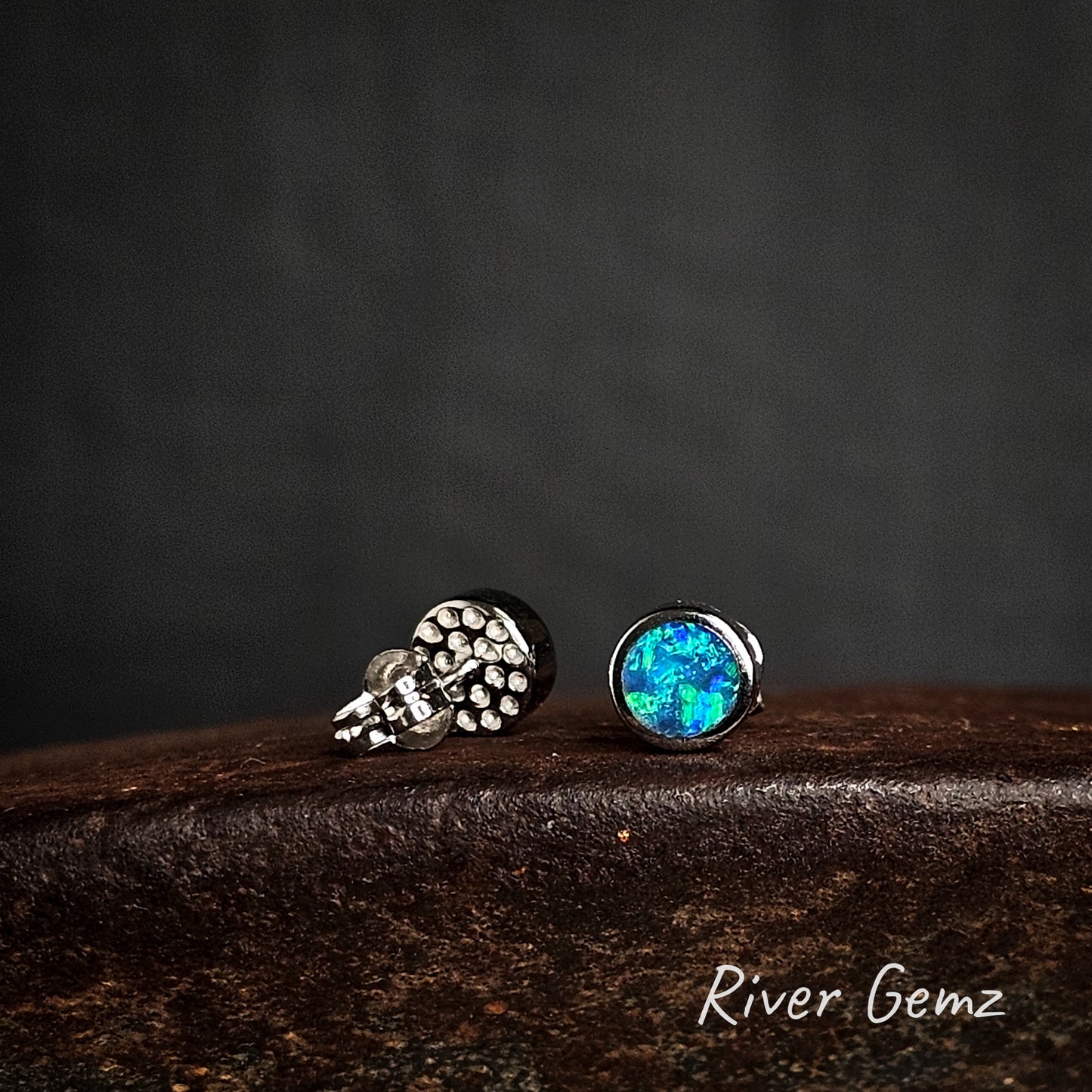Pair of silver earrings with black opals on a dark surface, branded 'River Gemz'.