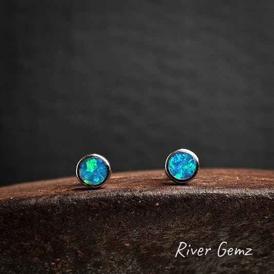 Opal stud earrings set in silver on a cast iron surface with 'River Gemz' branding.