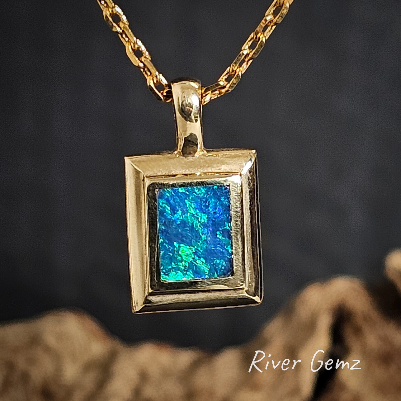 Gold pendant with blue and green opal on a dark background, featuring 'River Gemz' branding.