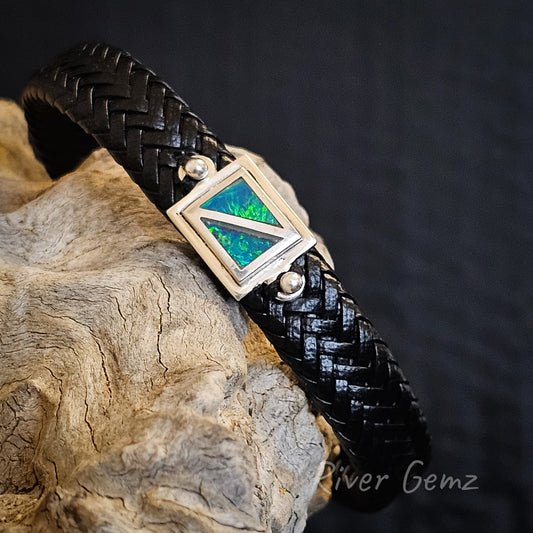 Two triangular shaped dark opals in a rectangular shaped silver setting attached to a black braided leather bracelet.