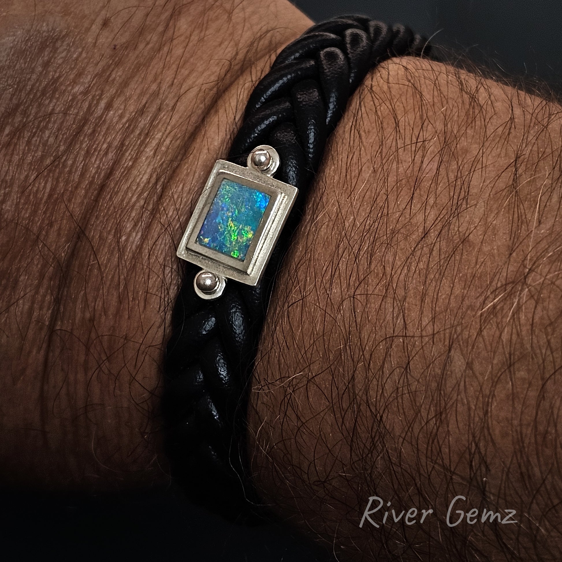 Black braided leather bracelet with a blue and green opal on a wrist, featuring 'River Gemz' branding.