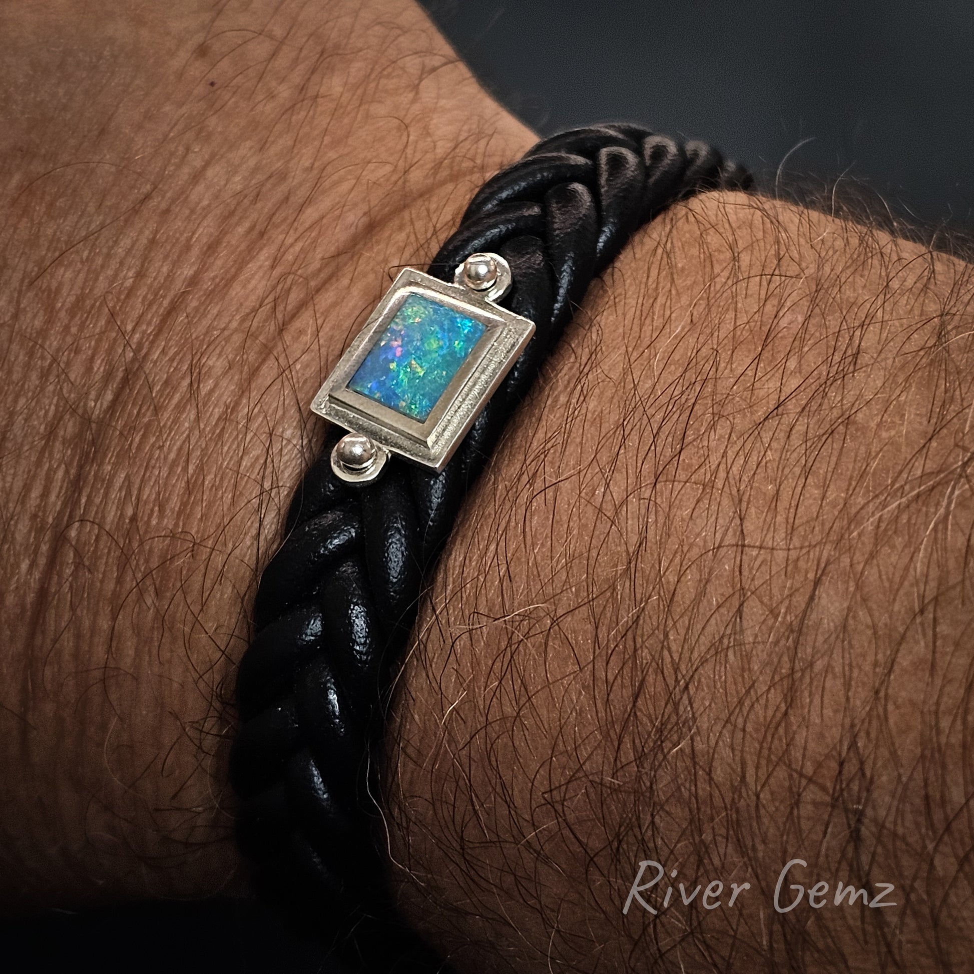 Black braided leather bracelet with a blue opal on a wrist, featuring 'River Gemz' branding.