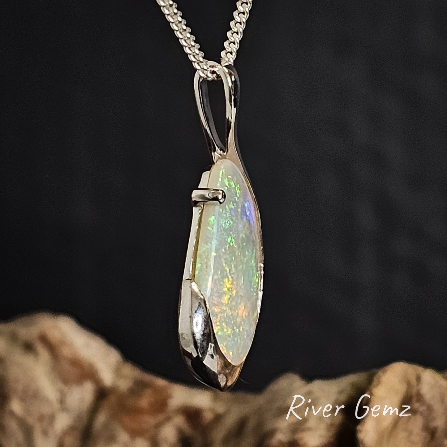 Side view of crystal opal pendant in silver necklace on a dark background with 'River Gemz' branding.