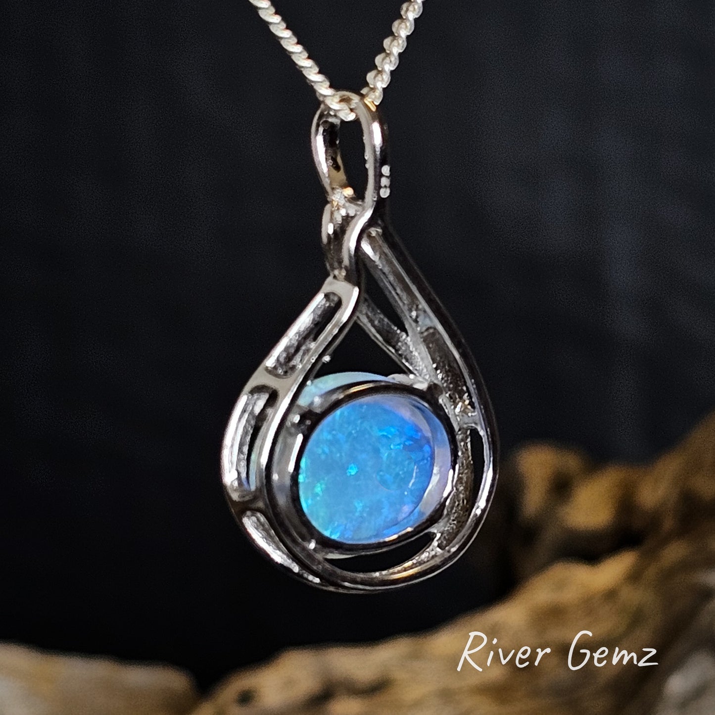 Back of the silver pendant showing the blues of the crystal opal continue throughout the stone on a dark background.