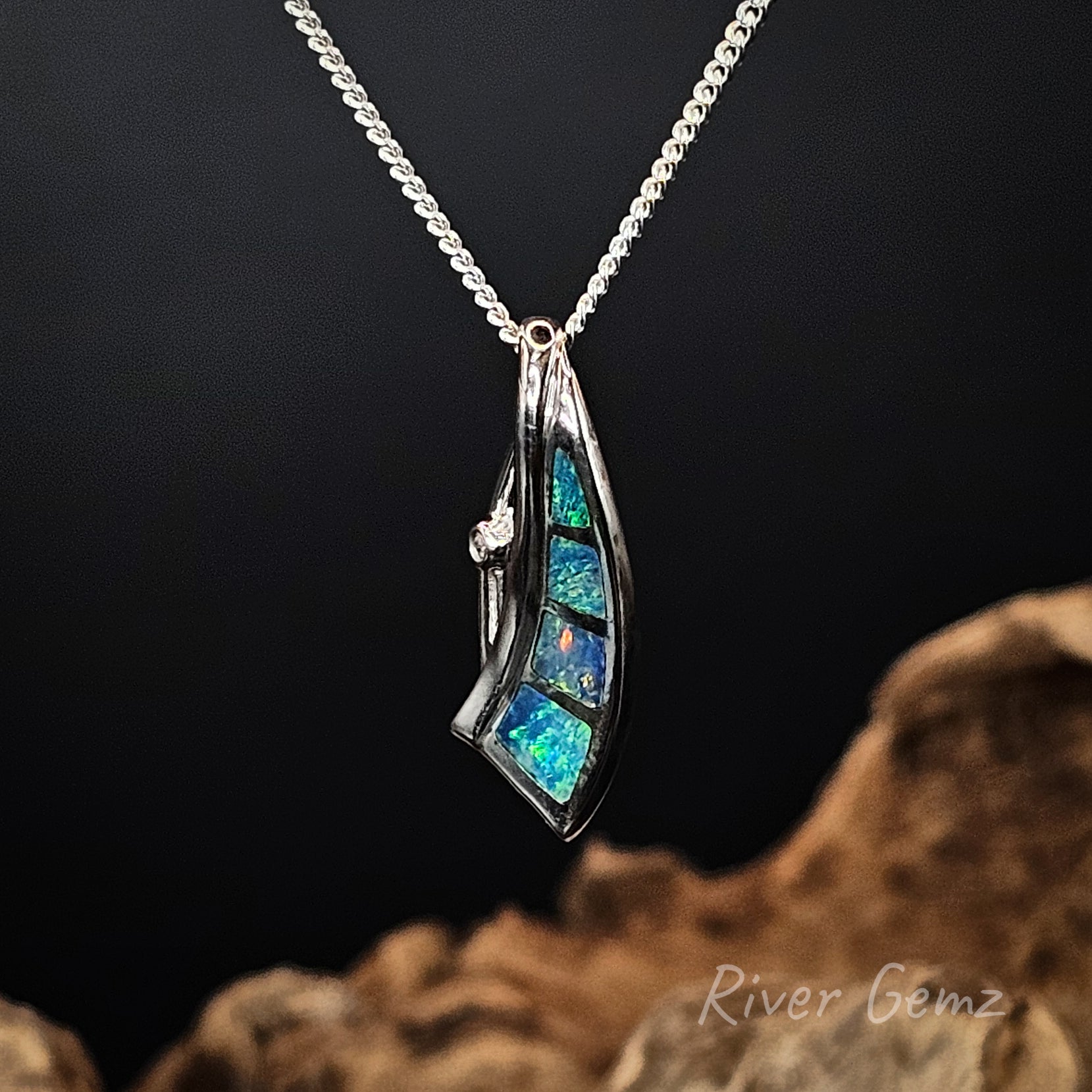 Silver necklace with 4 blue and green opals on a chain against a dark background