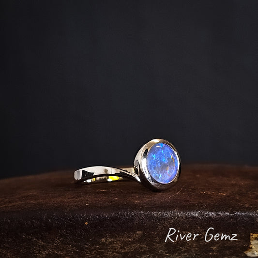 Silver ring with a blue round light opal on a dark background, branded 'River Gemz'.