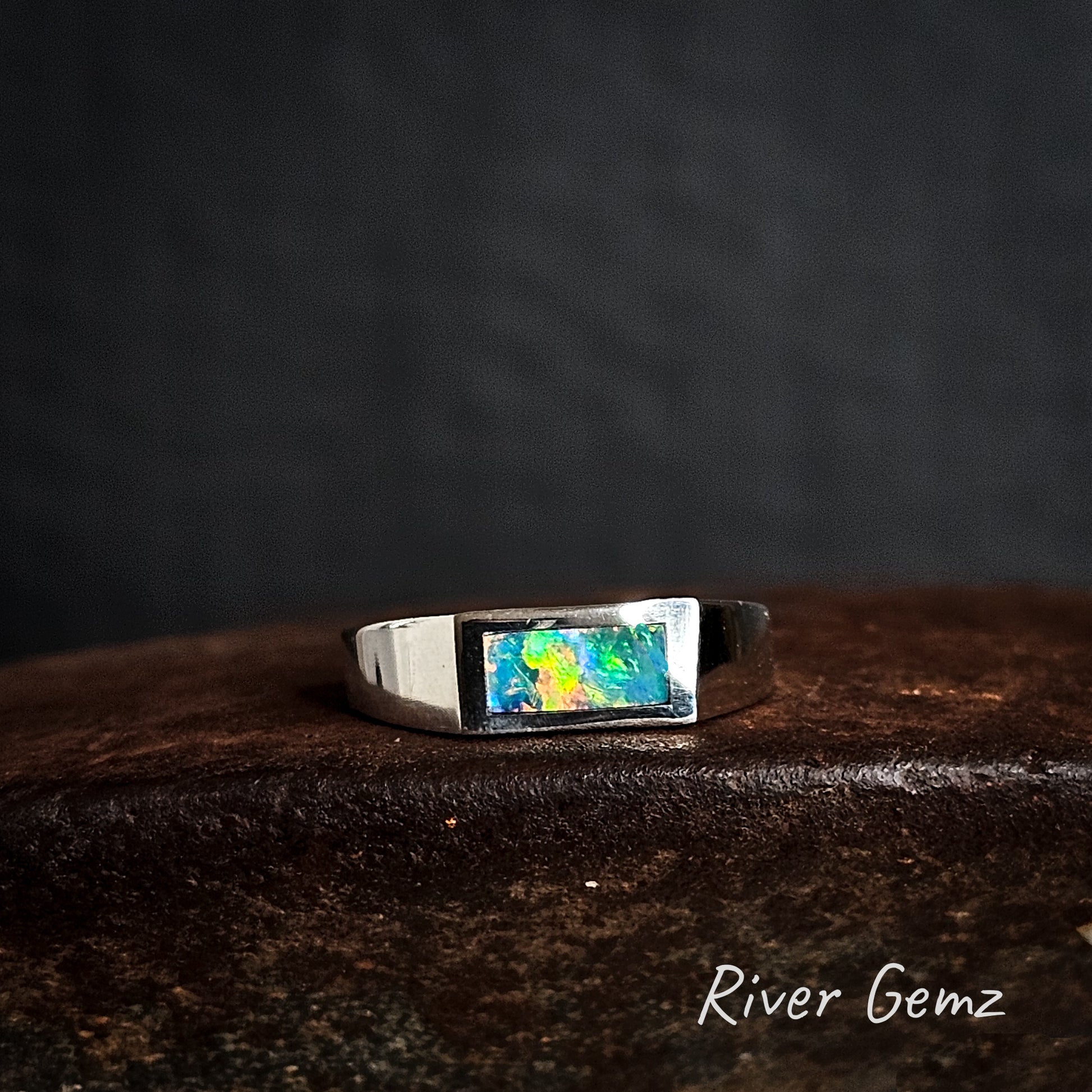 Silver ring with a multi-colour crystal opal on a dark background, branded 'River Gemz'.