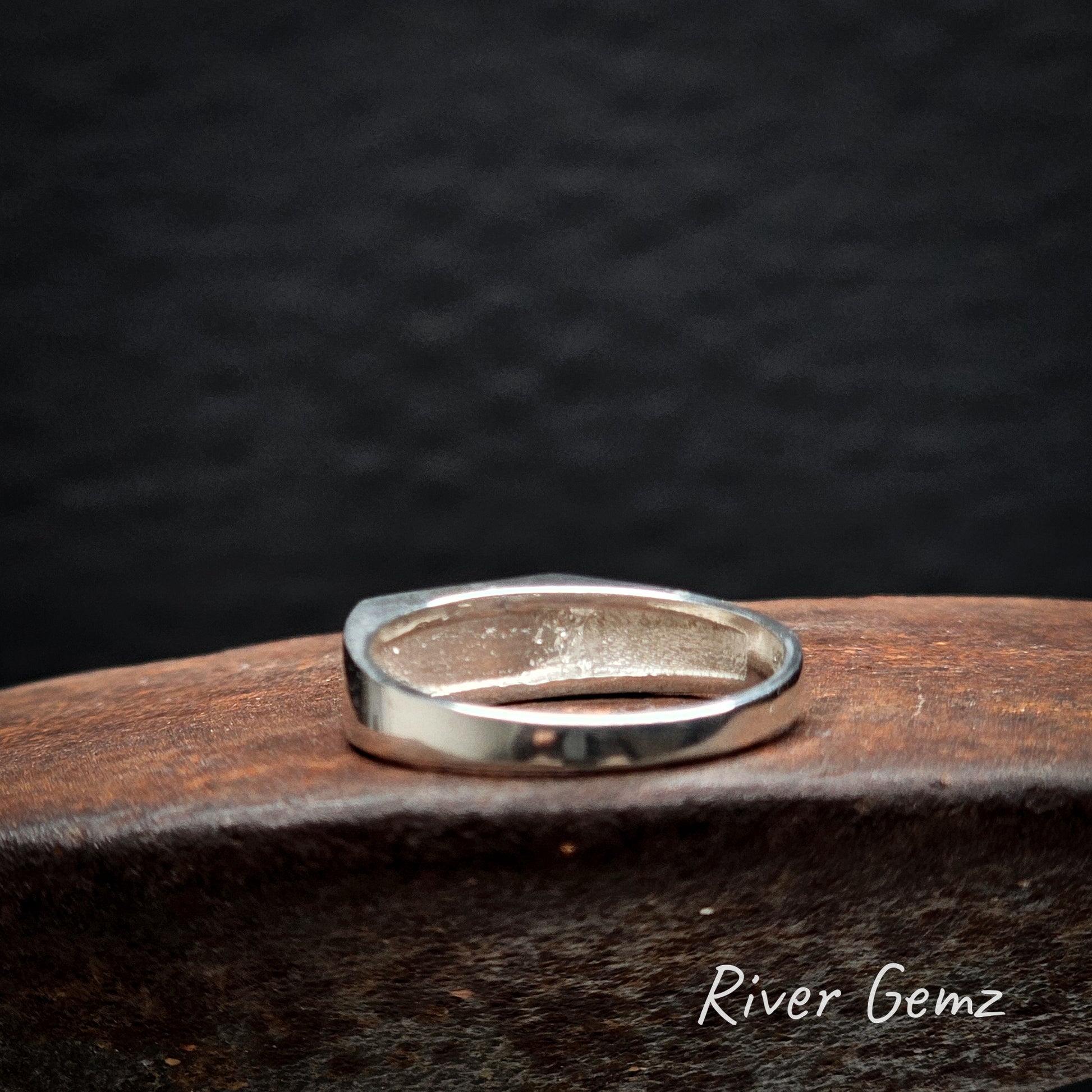 Rear view of silver ring on a dark textured surface with 'River Gemz' branding.
