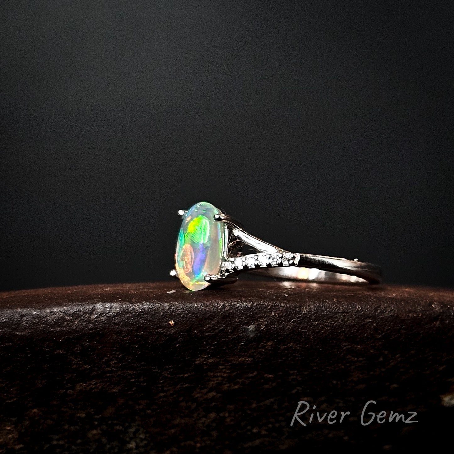 Ring with a colorful gemstone on a dark background, branded 'River Gemz'.