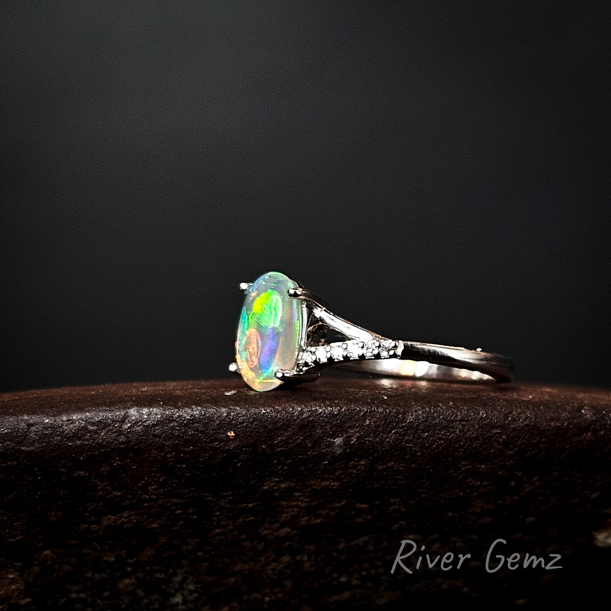 Ring with a colorful gemstone on a dark background, branded 'River Gemz'.