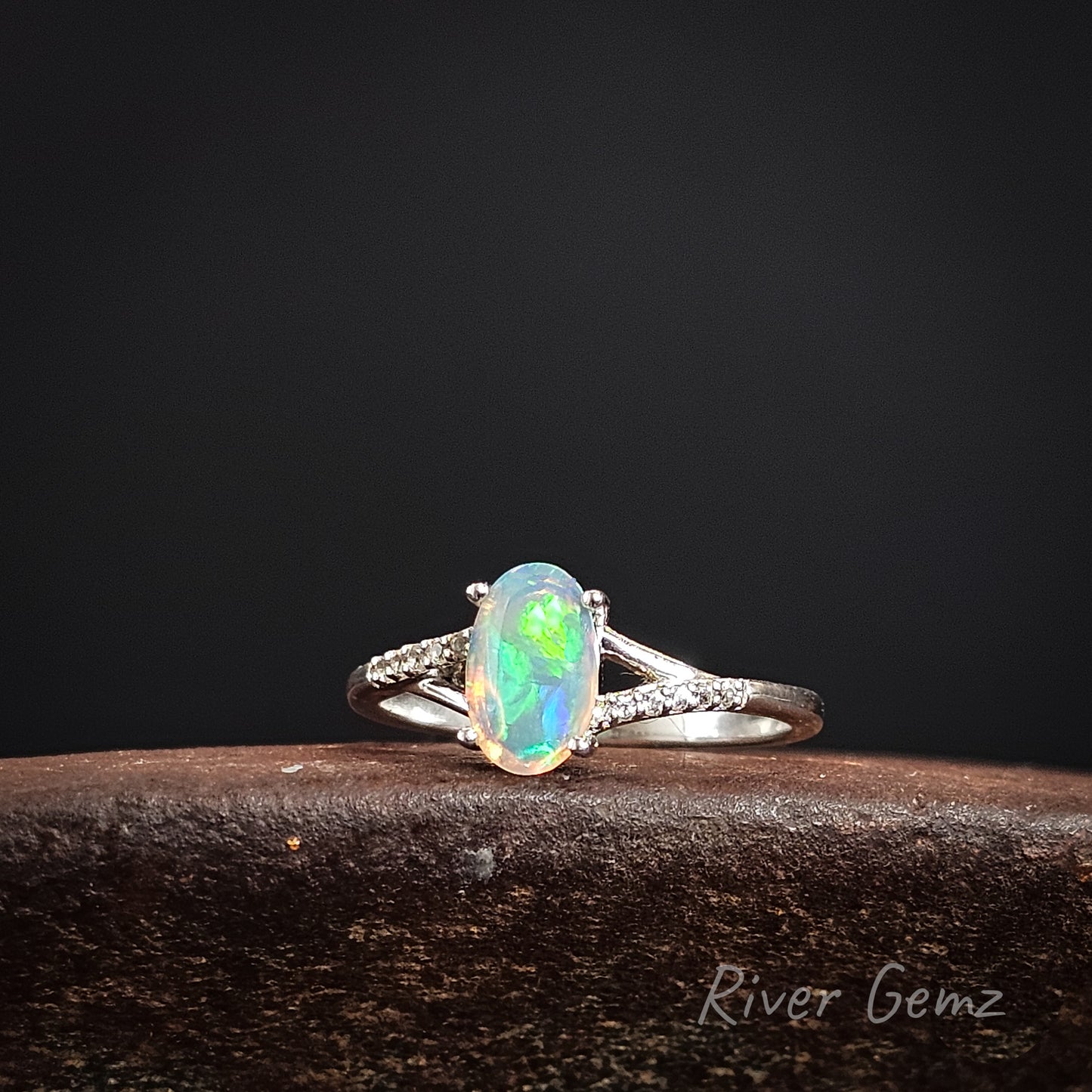 Opal ring with silver band on a dark background, featuring 'River Gemz' branding.