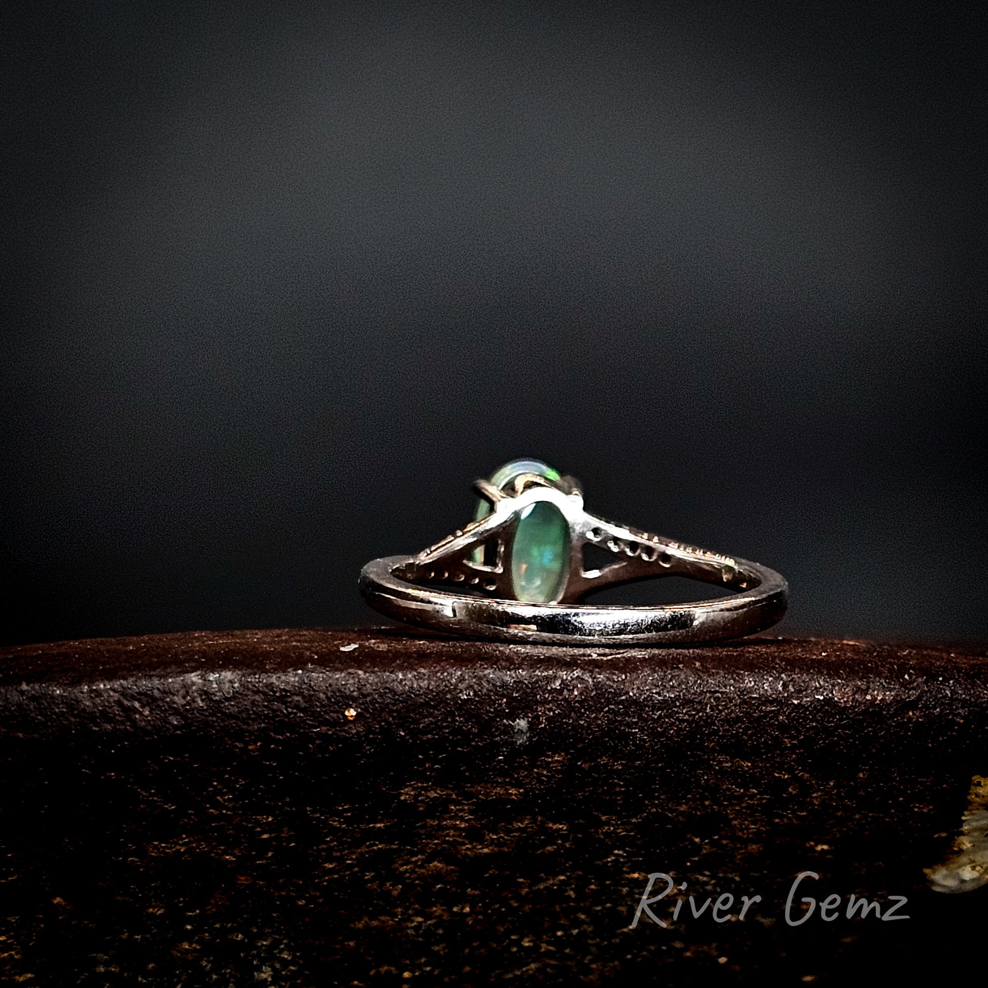 Rear view of silver ring with a green gemstone on a dark background, branded 'River Gemz'.