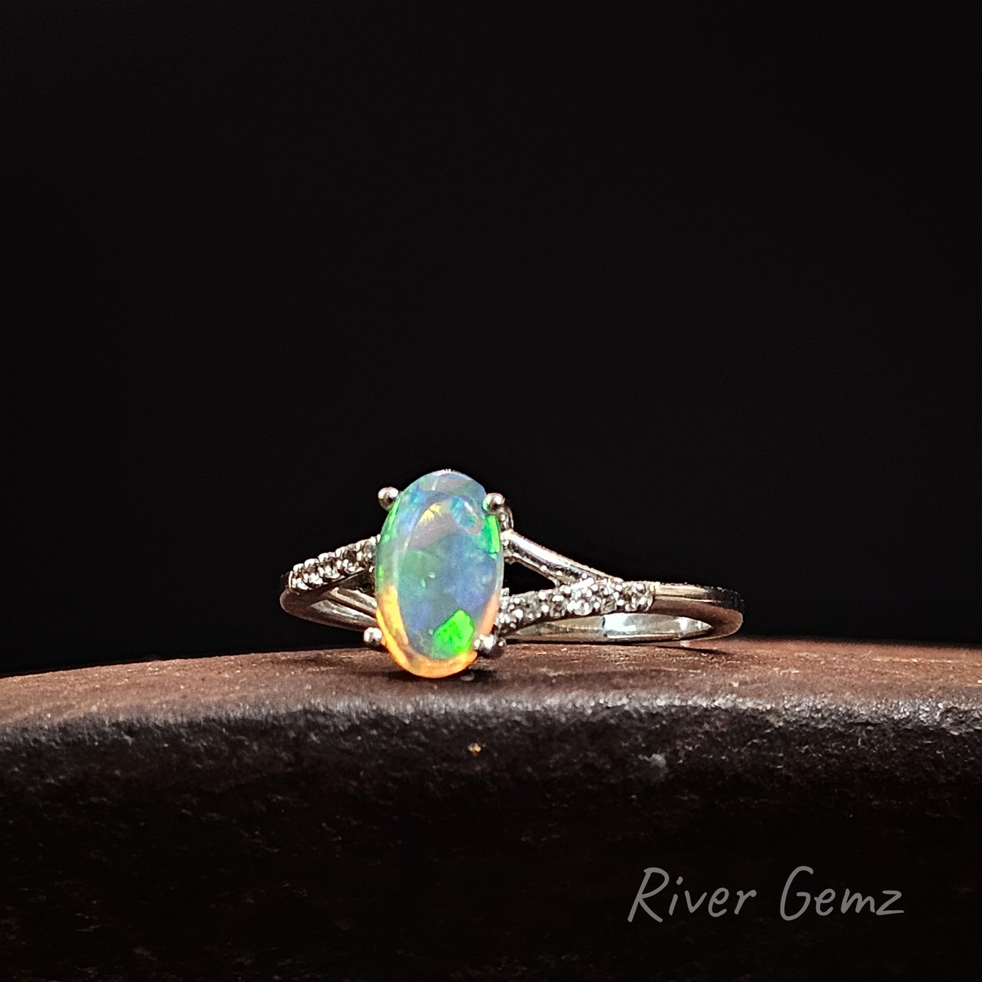 Opal ring with silver band on a dark background, featuring 'River Gemz' branding.