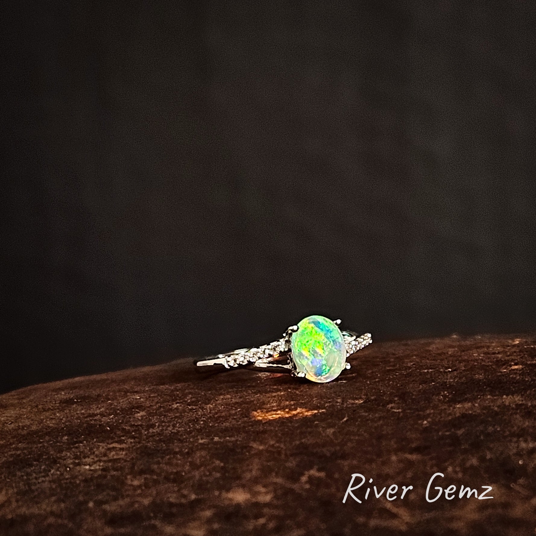 Opal and white topaz silver ring on a dark brown surface with 'River Gemz' branding.