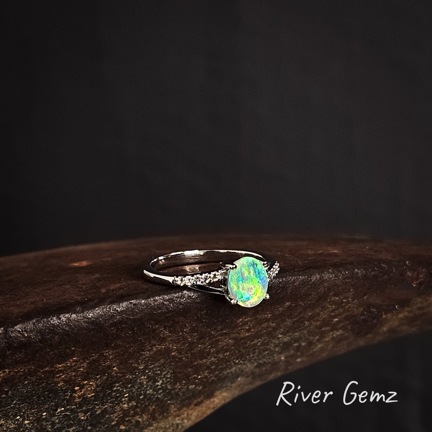 Ring with a green crystal opal and white topaz stones on the ring's shoulders on a dark background, featuring the brand 'River Gemz'.