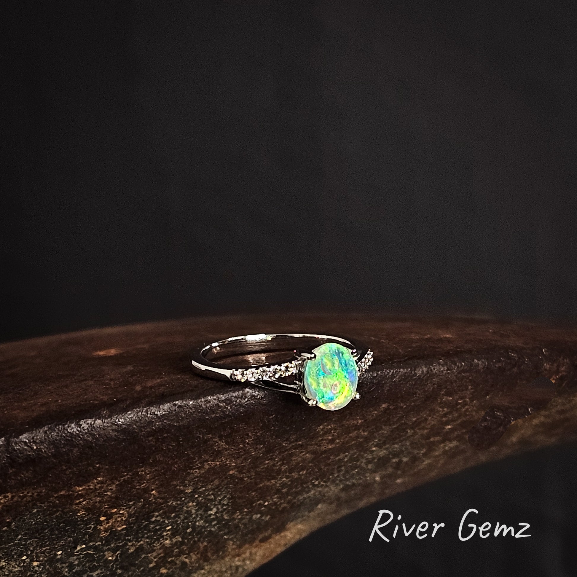 Ring with a green crystal opal and white topaz stones on the ring's shoulders on a dark background, featuring the brand 'River Gemz'.