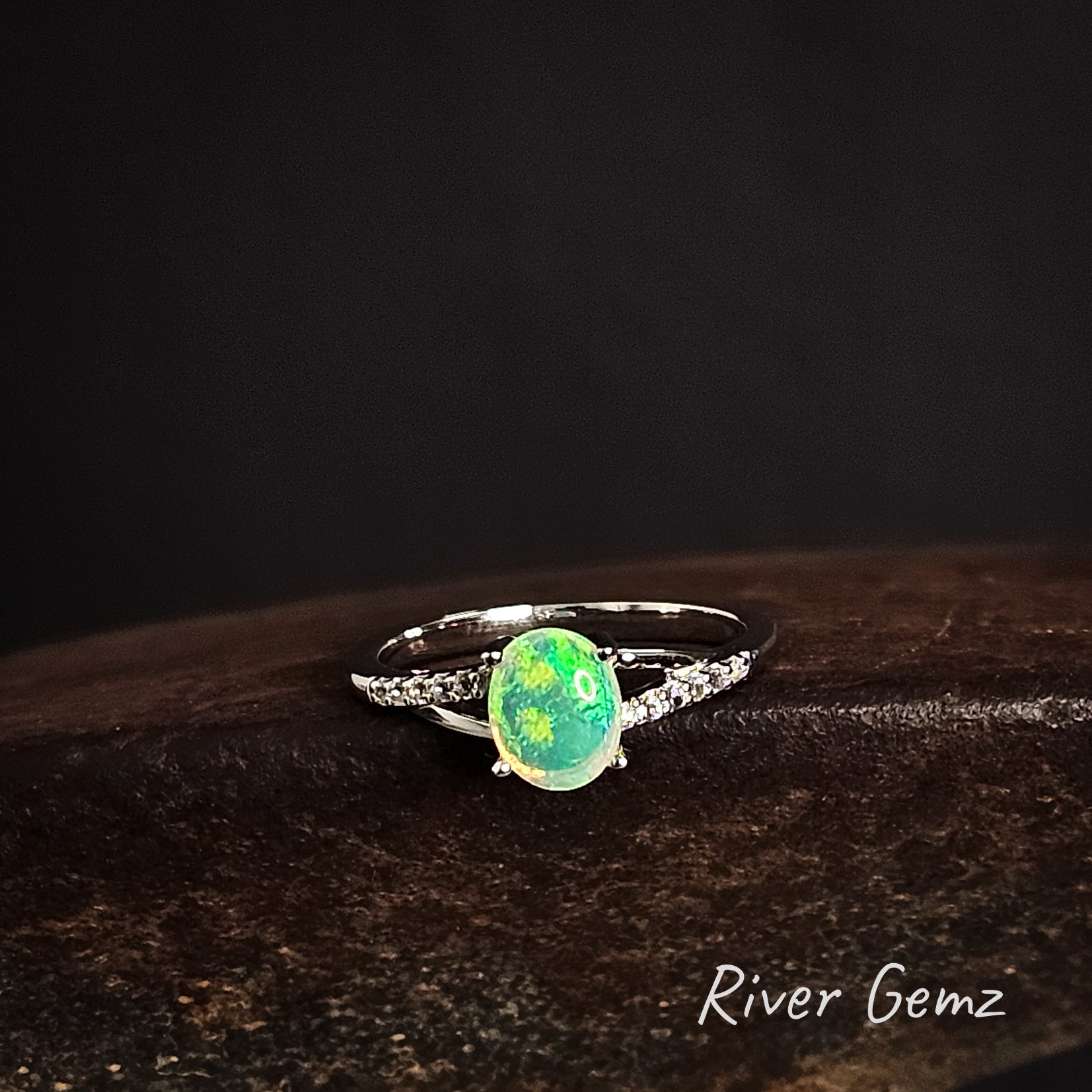 Ring with an oval shaped green opal stone on a dark background, branded 'River Gemz'.