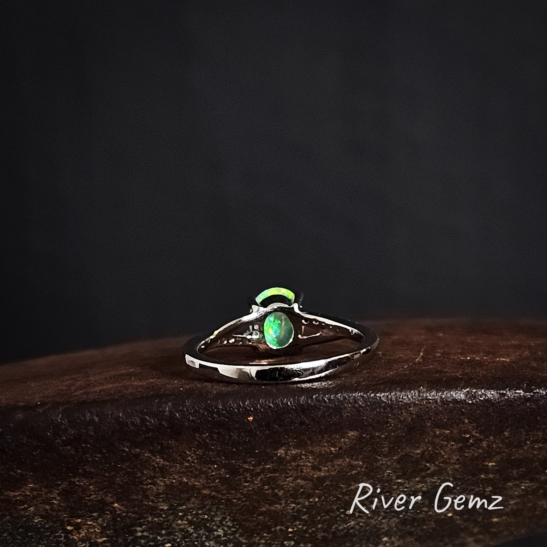 Rear of silver ring showing the green of the opal continues through the stone on a dark surface, branded 'River Gemz'.