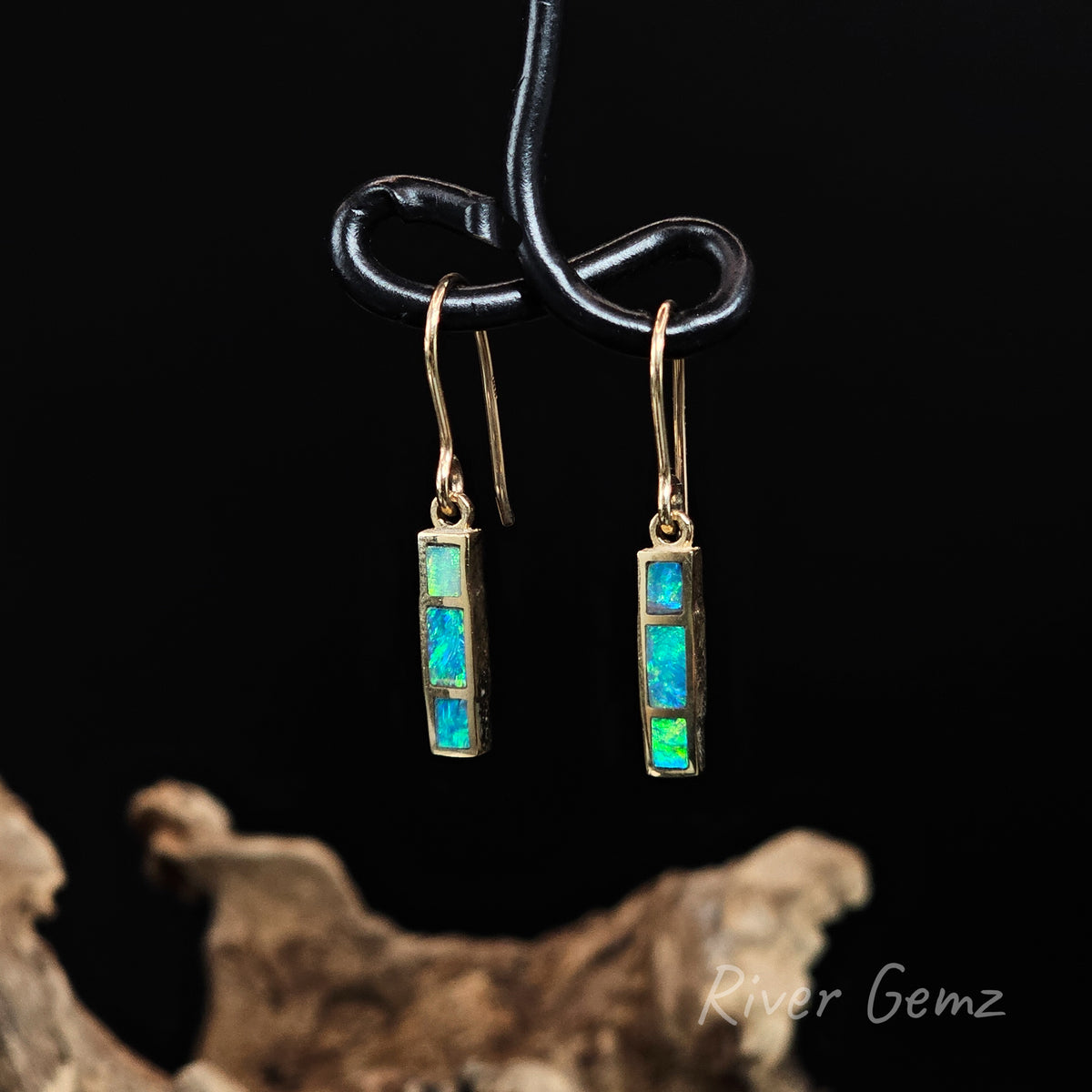 Three blue-green opals inlayed in yellow gold shepherd hooks against a black background.