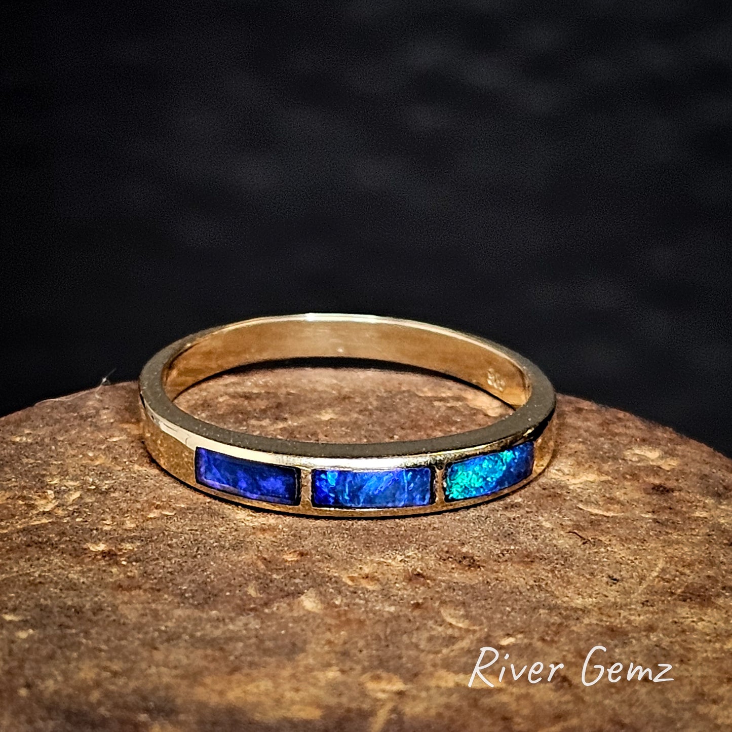 Gold ring with 3 rectangular shaped blue crystal opals on a dark background