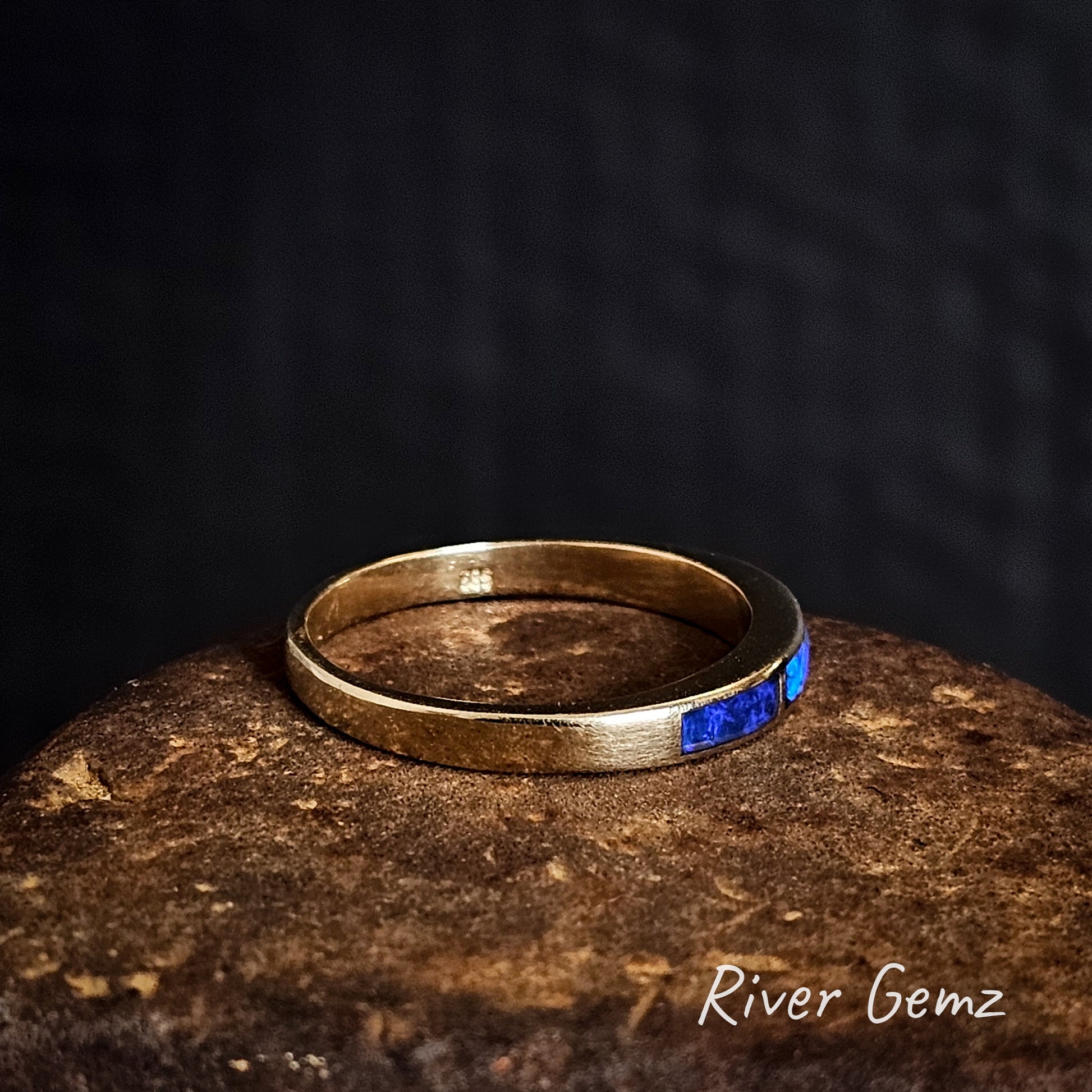 Side view of gold ring with inlayed opals on a dark background, branded 'River Gemz'.